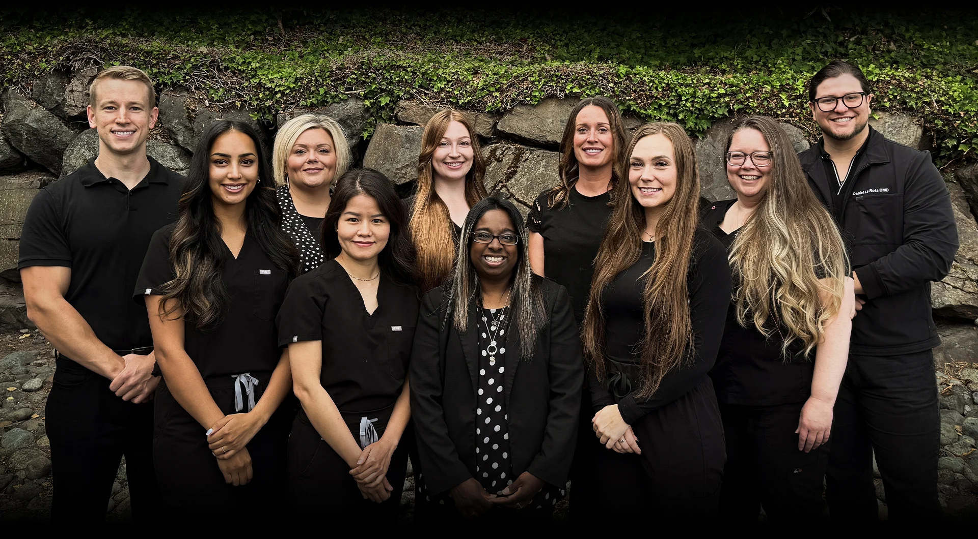 Team photo of staff at Travelle Family Dentistry office in Burien, WA standing outside in front of a garden